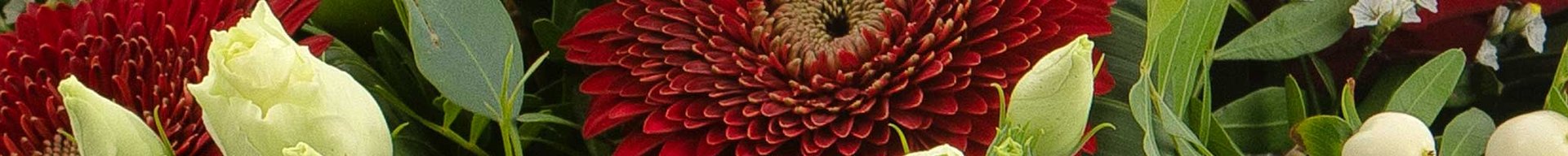 Et farverigt blomsterbuket med røde roser, hvide lysser og en dyb rød gerbera i midten. Grønne blade og små bær er også til stede, hvilket skaber en frodig og livlig sammensætning.